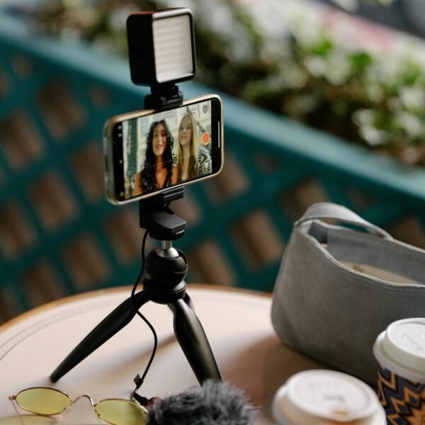 Two young vloggers recording a video blog in a café, enjoying coffee together with a smartphone and tripod setup.