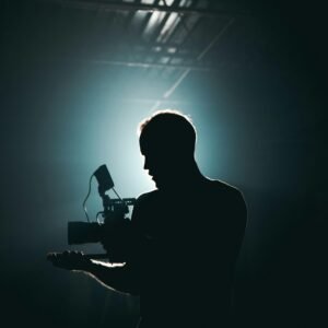 Silhouette of a cinematographer with camera gear in a dramatic, low light setting.